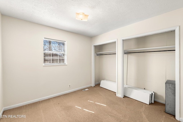 unfurnished bedroom featuring baseboards, visible vents, a textured ceiling, carpet flooring, and two closets