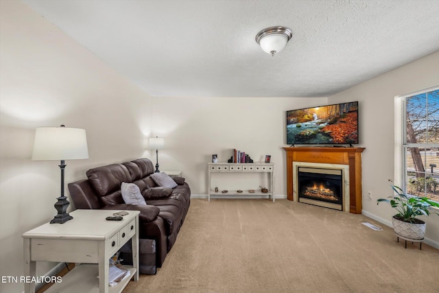 living room featuring visible vents, a textured ceiling, a glass covered fireplace, carpet floors, and baseboards