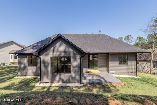 rear view of property featuring a yard, crawl space, a shingled roof, and a patio