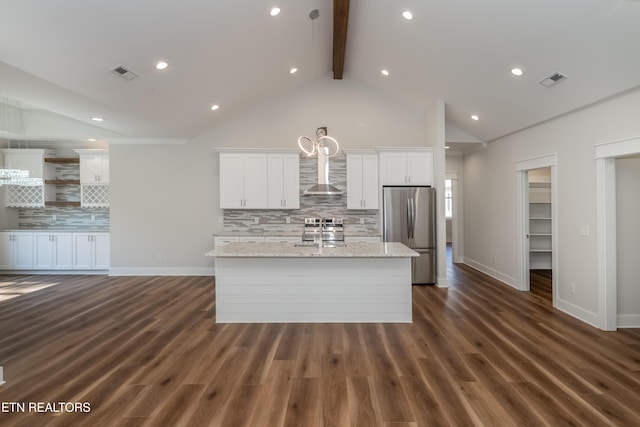 kitchen with visible vents, wall chimney range hood, an island with sink, freestanding refrigerator, and white cabinets