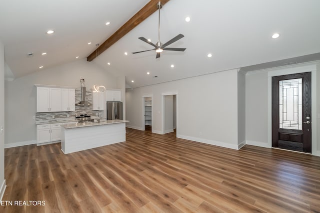 kitchen with beamed ceiling, an island with sink, open floor plan, and freestanding refrigerator