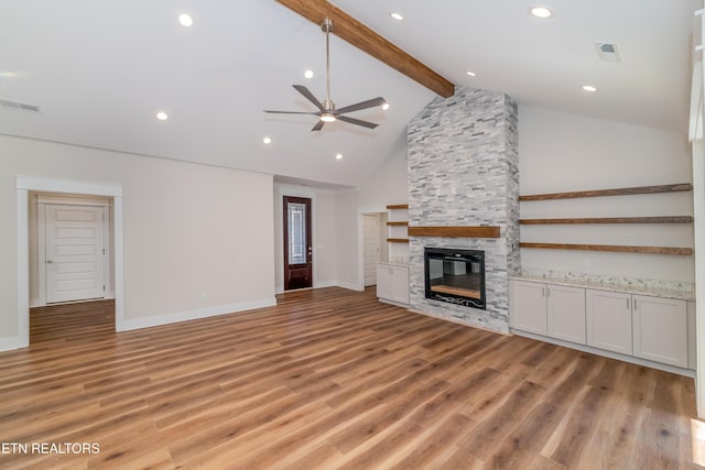 unfurnished living room with light wood finished floors, visible vents, beamed ceiling, a fireplace, and high vaulted ceiling