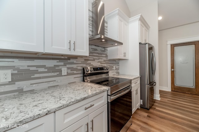 kitchen with white cabinetry, light wood-style floors, appliances with stainless steel finishes, wall chimney range hood, and decorative backsplash