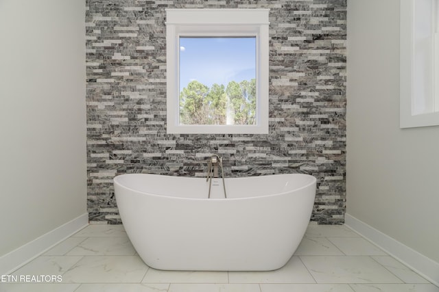 full bathroom with marble finish floor, baseboards, and a freestanding tub