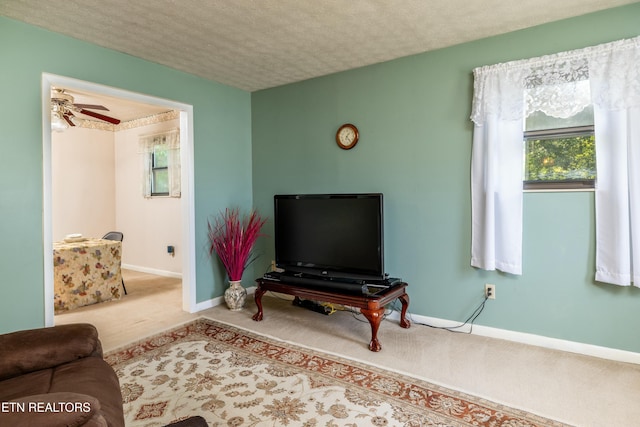 carpeted living area with a ceiling fan, baseboards, and a textured ceiling