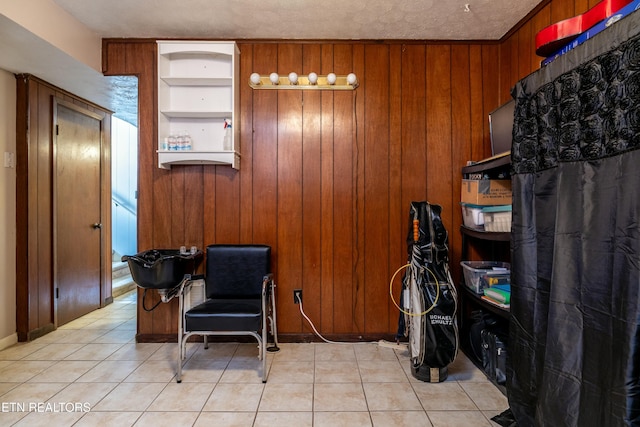 sitting room featuring light tile patterned flooring, wood walls, built in shelves, and a textured ceiling