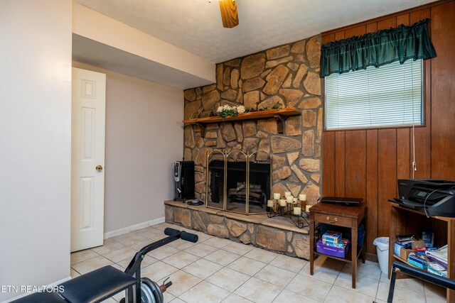 living area featuring a stone fireplace, light tile patterned flooring, baseboards, and ceiling fan