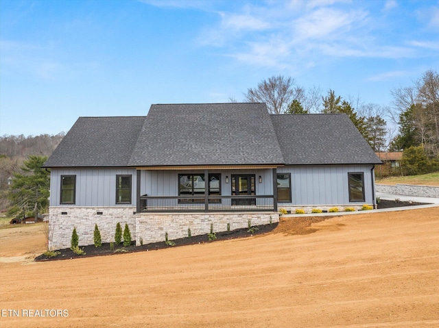 modern farmhouse style home with a porch, stone siding, board and batten siding, and roof with shingles