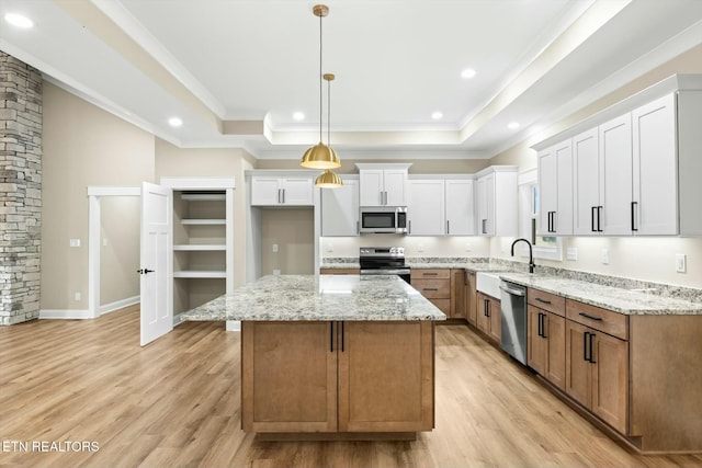 kitchen featuring stainless steel appliances, light wood-style floors, a tray ceiling, and ornamental molding