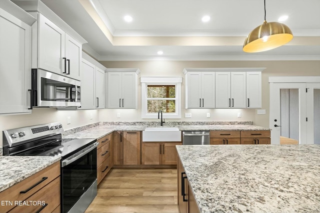 kitchen with a tray ceiling, ornamental molding, appliances with stainless steel finishes, light wood-style floors, and a sink