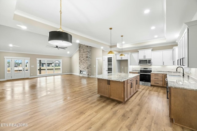 kitchen featuring open floor plan, light wood-style floors, stainless steel appliances, a raised ceiling, and a ceiling fan