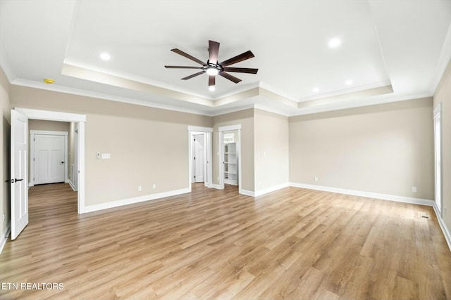 empty room with a tray ceiling, light wood-style floors, ornamental molding, and a ceiling fan