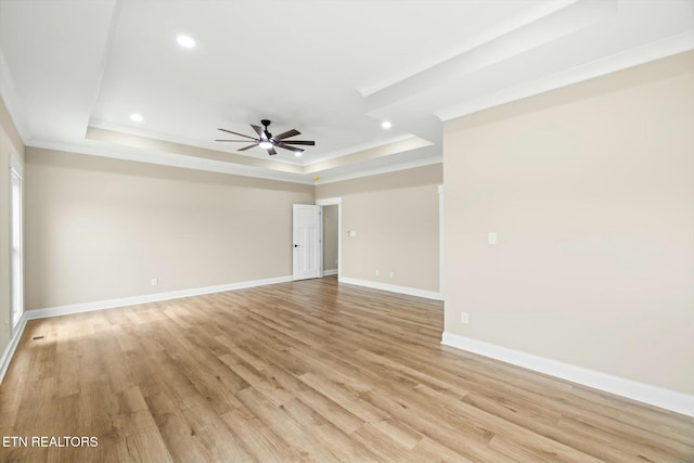 spare room with a ceiling fan, baseboards, light wood finished floors, a tray ceiling, and crown molding