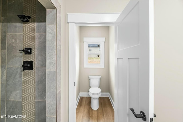 bathroom featuring a tile shower, toilet, baseboards, and wood finished floors