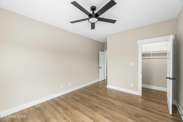 unfurnished bedroom featuring a closet, light wood-style flooring, a walk in closet, and baseboards