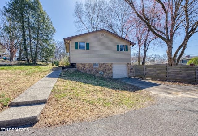 view of side of property featuring an attached garage, fence, a yard, and driveway