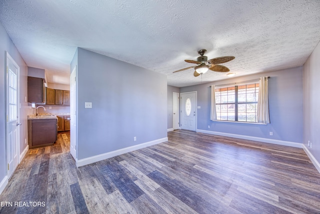 unfurnished living room with dark wood finished floors, a ceiling fan, baseboards, and a sink