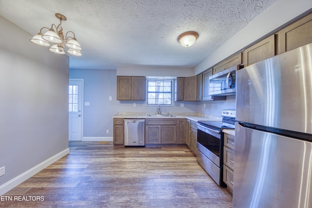 kitchen featuring baseboards, light wood finished floors, a sink, appliances with stainless steel finishes, and a textured ceiling