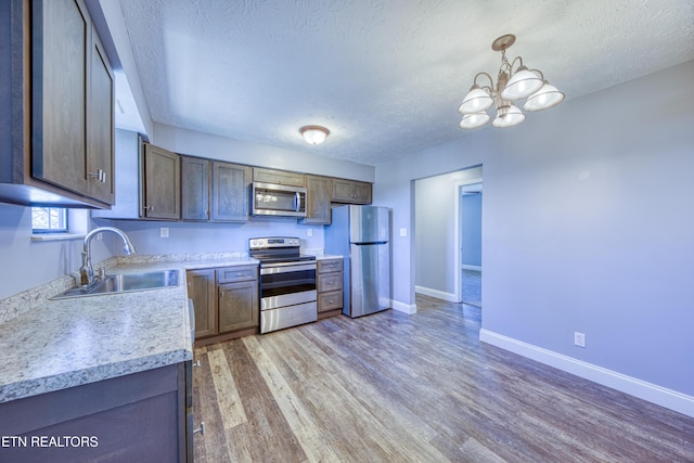 kitchen featuring baseboards, a sink, light countertops, appliances with stainless steel finishes, and light wood-type flooring