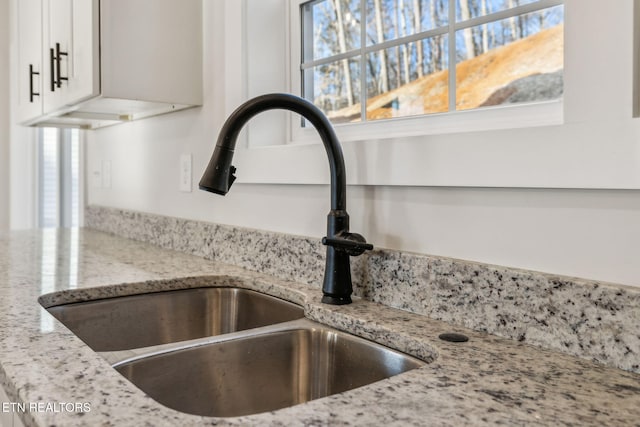 interior details featuring light stone counters, white cabinets, and a sink