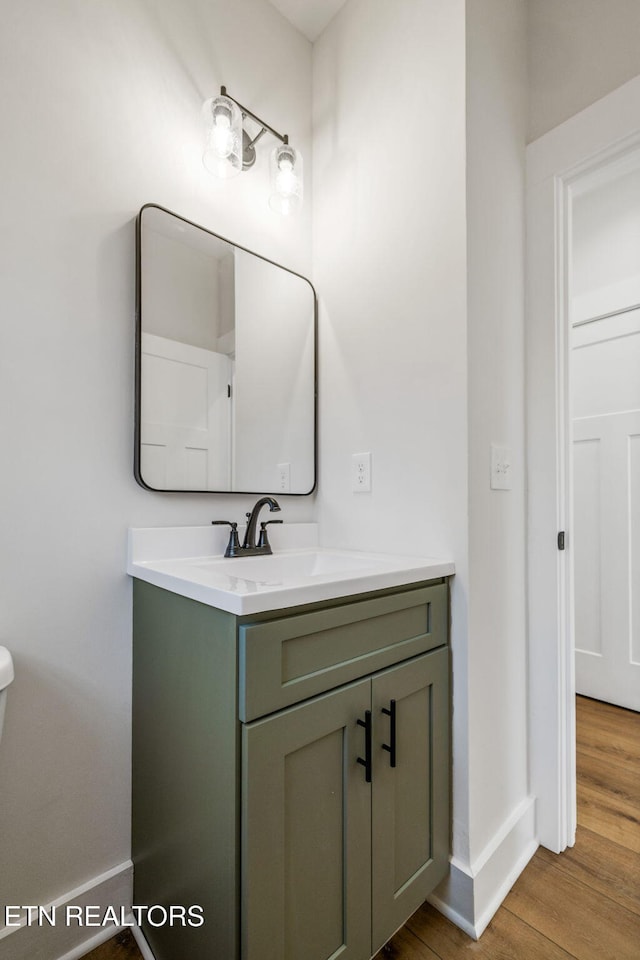 half bathroom with toilet, vanity, baseboards, and wood finished floors