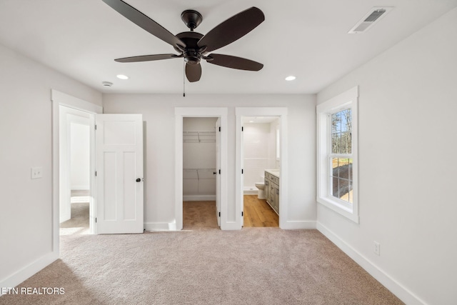 unfurnished bedroom featuring a walk in closet, light colored carpet, visible vents, and baseboards