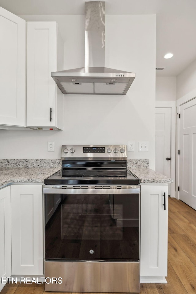 kitchen with light wood-style flooring, light stone counters, white cabinetry, stainless steel electric range, and wall chimney exhaust hood