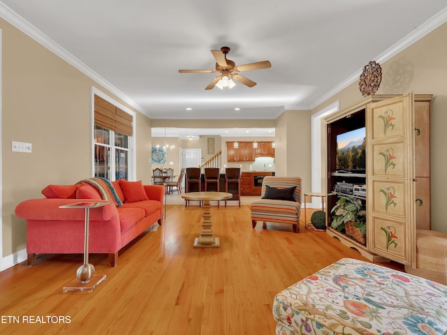 living area featuring baseboards, ceiling fan with notable chandelier, light wood-type flooring, and ornamental molding