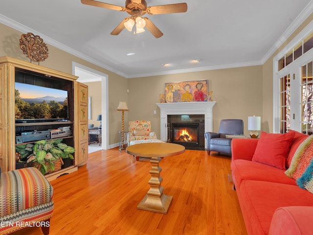 living area with a glass covered fireplace, a ceiling fan, light wood finished floors, and ornamental molding