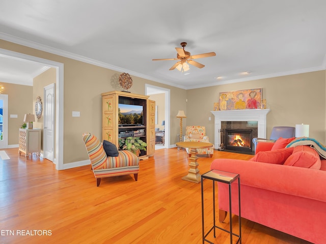 living area featuring crown molding, baseboards, a fireplace with flush hearth, light wood-style flooring, and a ceiling fan