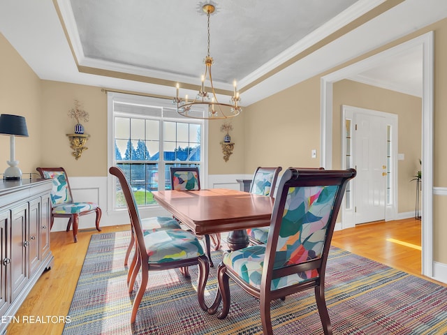 dining room with light wood finished floors, a wainscoted wall, crown molding, and a tray ceiling