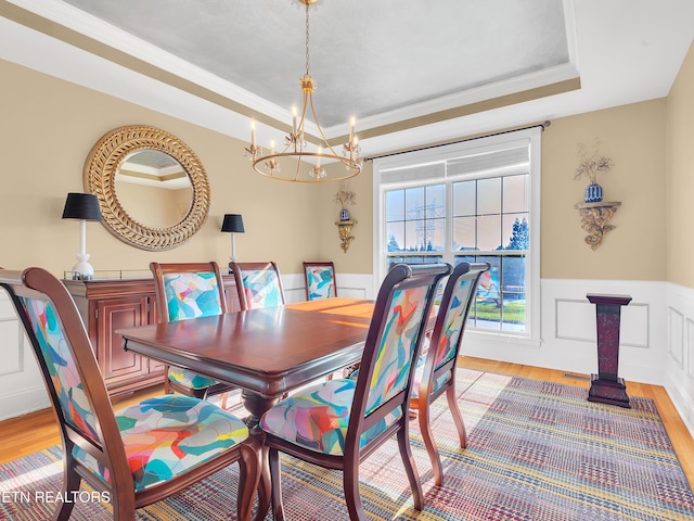 dining room featuring a tray ceiling, light wood-style flooring, and a wainscoted wall