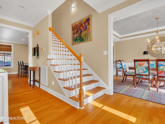 staircase featuring visible vents, ornamental molding, an inviting chandelier, and wood finished floors