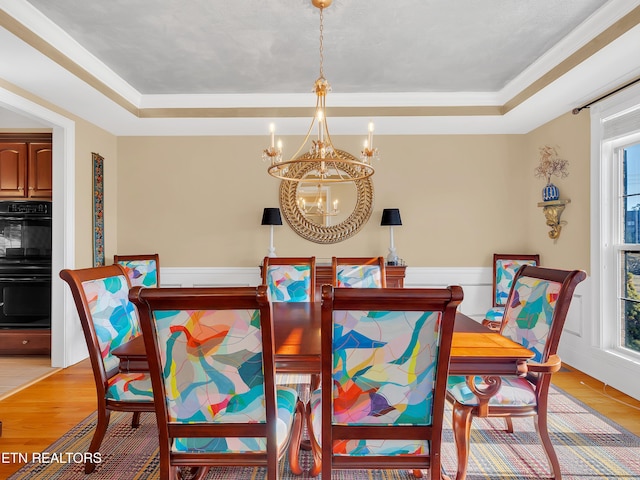 dining area with a notable chandelier, light wood-style flooring, plenty of natural light, and a tray ceiling