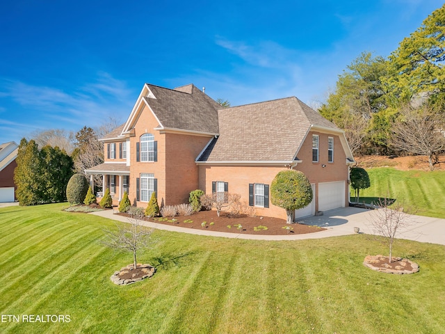 traditional-style home featuring concrete driveway, an attached garage, a front yard, and roof with shingles