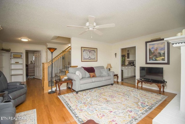 living room with crown molding, ceiling fan, stairs, light wood-style flooring, and a textured ceiling