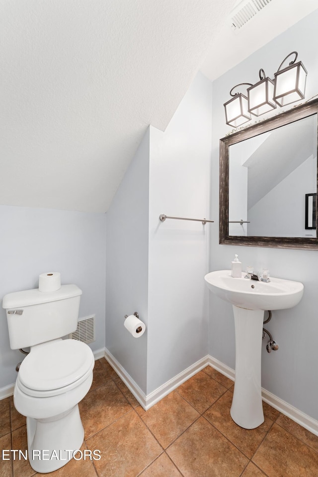 bathroom featuring visible vents, toilet, a textured ceiling, baseboards, and vaulted ceiling