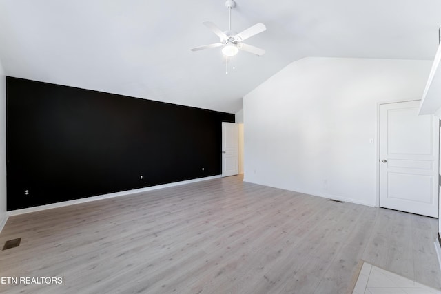 spare room with visible vents, light wood-style flooring, a ceiling fan, baseboards, and vaulted ceiling