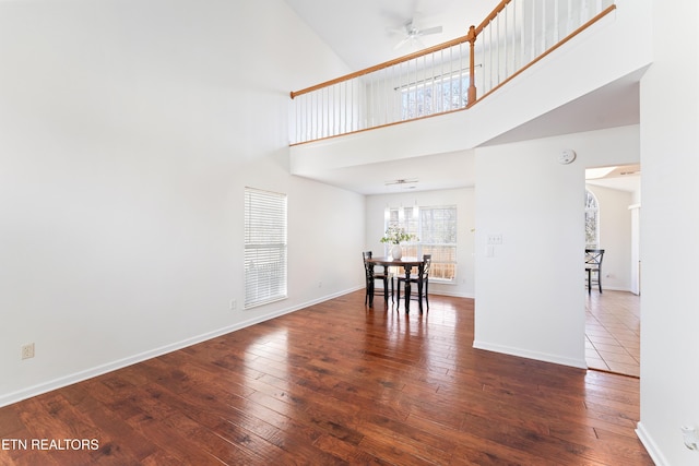 unfurnished dining area featuring ceiling fan, baseboards, a high ceiling, and hardwood / wood-style floors