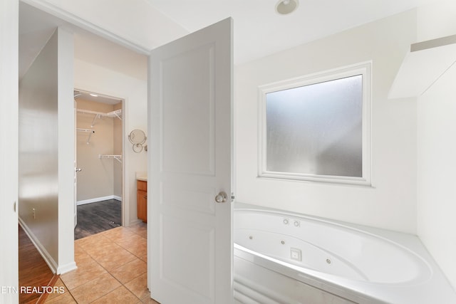 bathroom featuring vanity, a tub with jets, baseboards, a walk in closet, and tile patterned floors