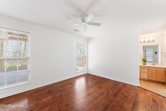 unfurnished bedroom with visible vents, connected bathroom, baseboards, hardwood / wood-style floors, and a ceiling fan