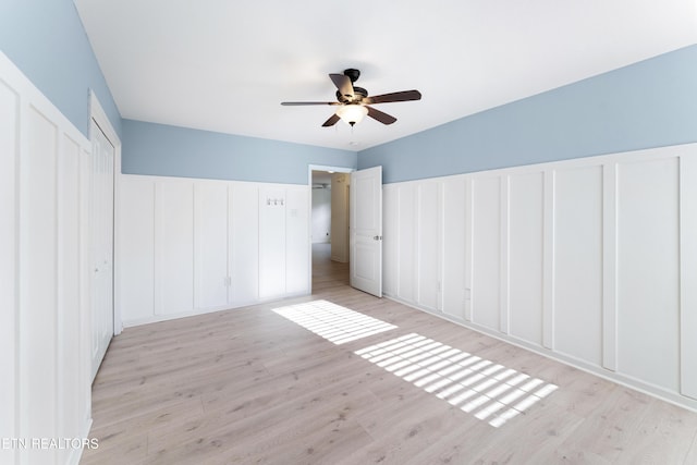 unfurnished bedroom featuring a wainscoted wall, a decorative wall, a ceiling fan, and light wood-type flooring