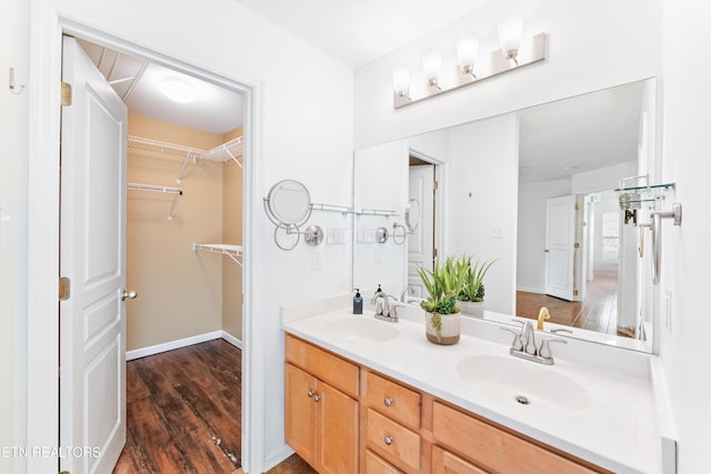 full bathroom featuring a sink, a walk in closet, wood finished floors, and double vanity