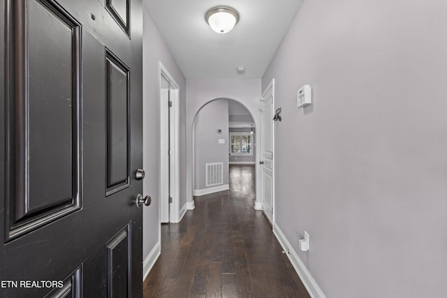 corridor with visible vents, arched walkways, baseboards, and dark wood-style flooring