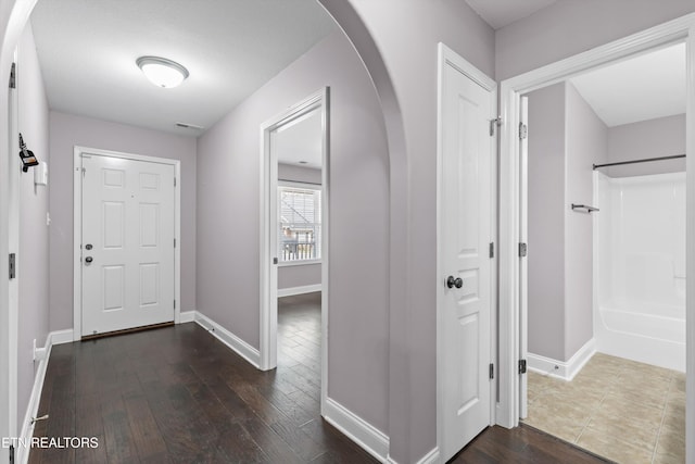hall with arched walkways, visible vents, dark wood-type flooring, and baseboards