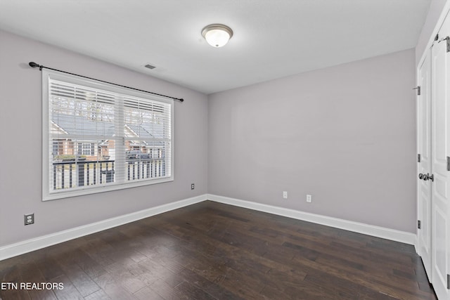 spare room featuring dark wood finished floors, visible vents, and baseboards