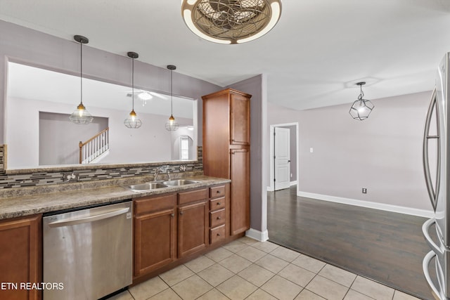kitchen featuring a sink, decorative backsplash, stainless steel appliances, pendant lighting, and brown cabinets