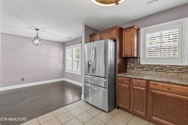 kitchen featuring light tile patterned floors, baseboards, brown cabinets, stainless steel fridge, and tasteful backsplash