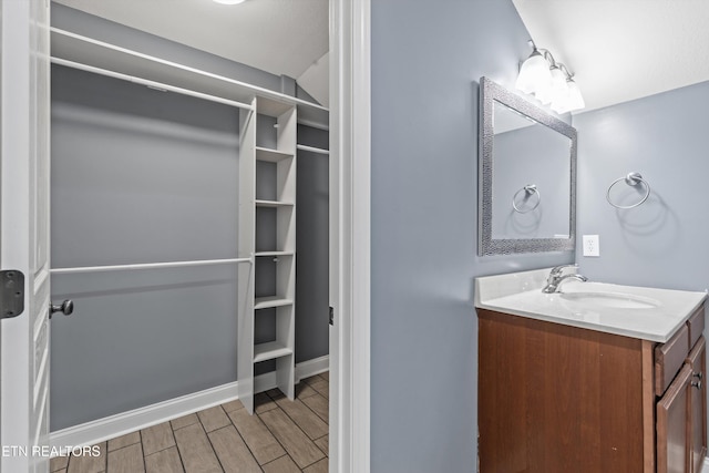 bathroom with vanity, a walk in closet, baseboards, and wood finish floors