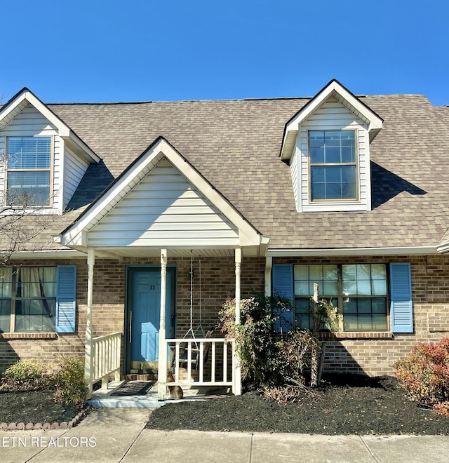 new england style home featuring brick siding, covered porch, and a shingled roof